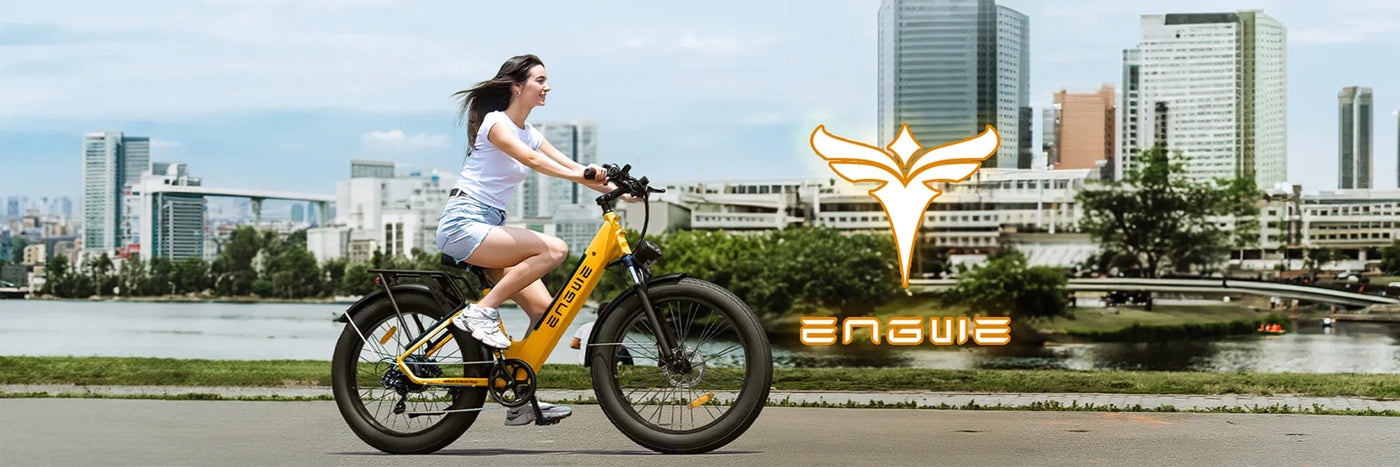 Woman joyfully riding a yellow ENGWE electric bike along a city riverfront, with urban skyscrapers in the background, exemplifying eco-friendly urban transportation.